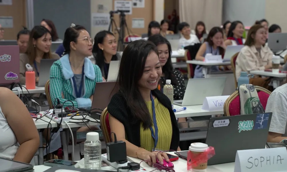Participants at laptops during a Digital X Bootcamp session, laughing while building on their own machines