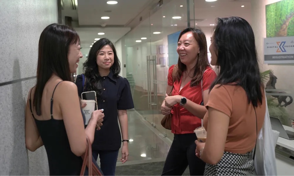 Four participants talking in the corridor outside the Digital X Bootcamp registration desk